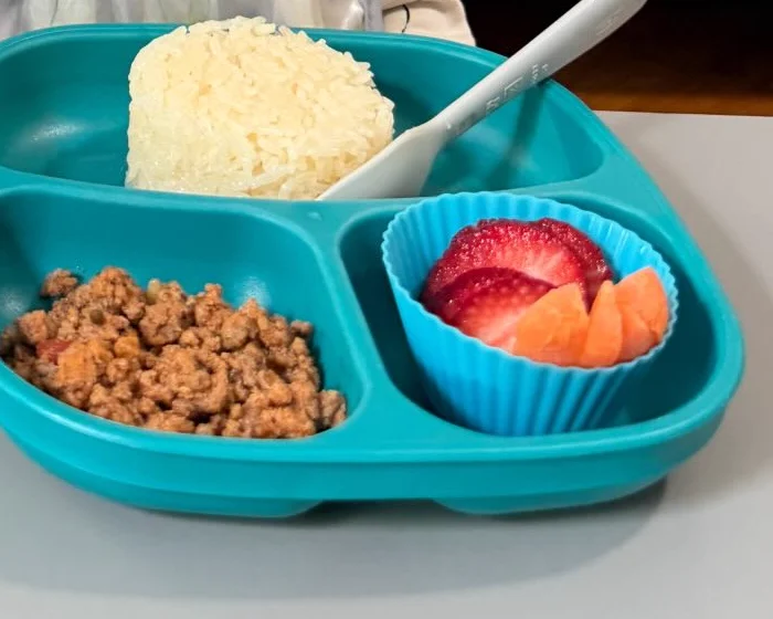 Almuerzo servido en Creative Minds: arroz, carne molida, fresas y fruta en un plato turquesa